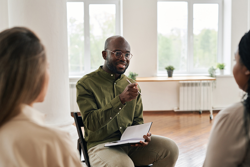 Young confident black man with notebook pointing at one of patients