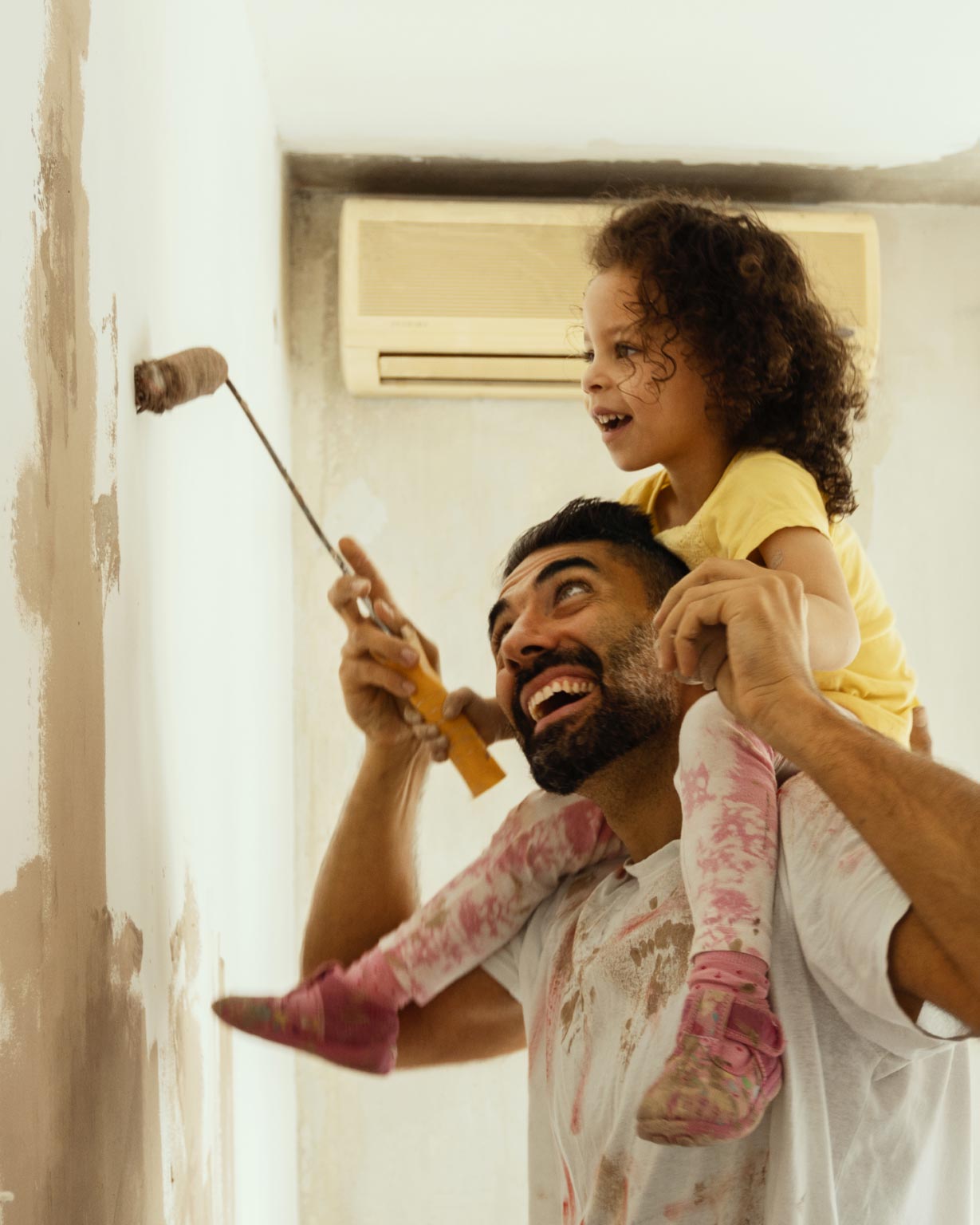 Daughter on father's shoulders painting a wall in their house