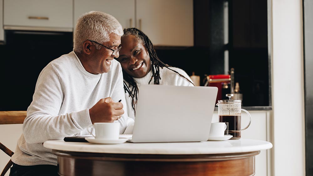Retired couple in front of computer in kitchen drinking coffee